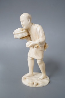 A Japanese carved ivory figure, Meiji period, modelled as a fruit vendor carrying a bowl of fruit in one hand and a piece of fruit in the other, standing on a naturalistic circular base, signed on base, height 14.5cm